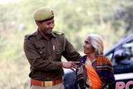 Projects A smiling Indian police officer assists an elderly woman outdoors, showcasing community care.