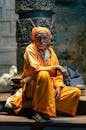 Projects Elderly man in a yellow gown sitting by a temple column, symbolizing spirituality.