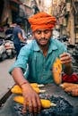Projects Man grilling corn on coals in lively Indian street market scene.